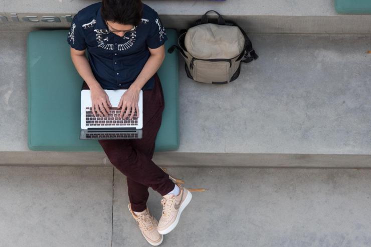 Person sitting on a cement bench on their laptop