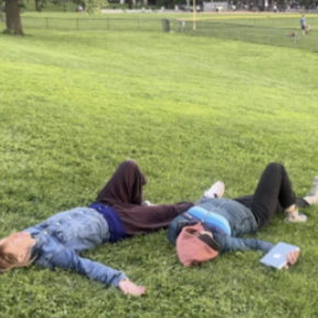 two people lying on the grass in similar positions, one holding a book