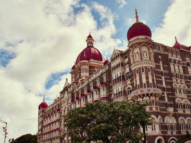 A large red brick hotel with rounded dome roofs and white windows with a blue sky and clouds