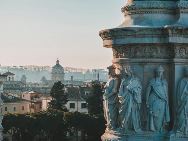 A large stone pillar on the right, the left a the Rome skyline and sunset