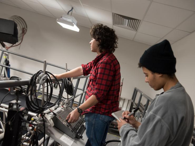 One student working with sound equipment while other student is taking notes