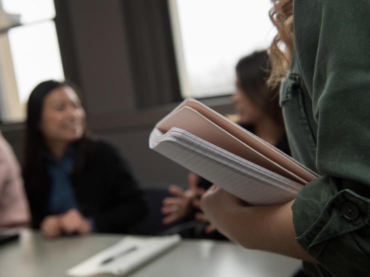 Close-up of notebook in student's arm with blurred students in the background