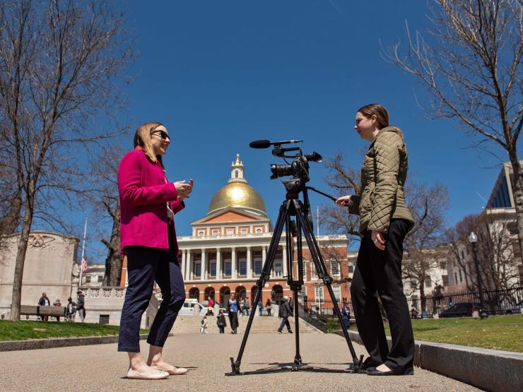 Someone being filmed on camera in front of the Boston State House