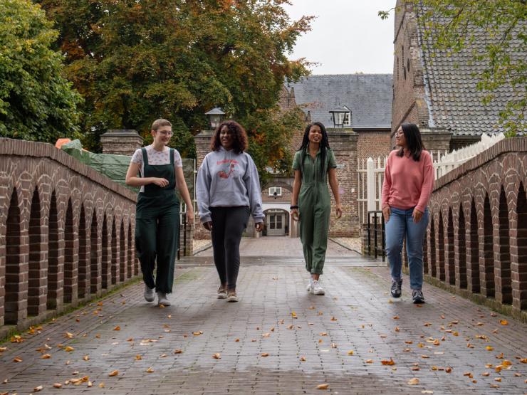 4 students walk across the brick bridge