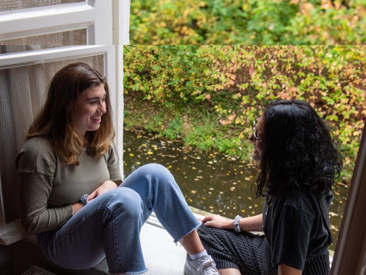 2 students sit on the window ledge talking