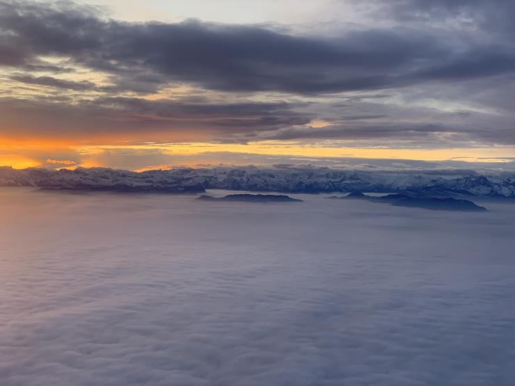 View of a sunrise rising over snow-peaked mountains and the clouds