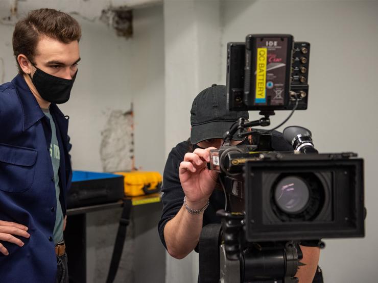 A student handles a camera while another student oversees