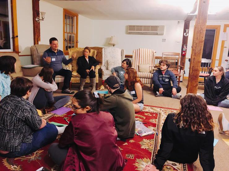 Students gathered for a spiritual retreat, sitting cross-legged on a red rug