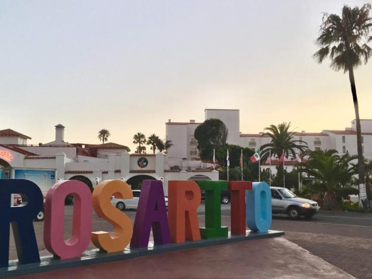 Colorful signing reading "Rosarito" in Rosarito, Mexico with buildings and a palm tree in the background