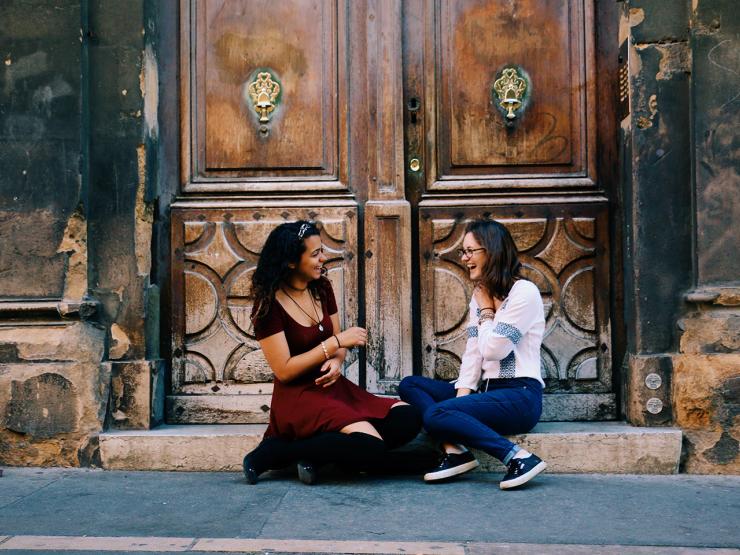 Two students sitting facing each other on a step in front of wooden doors in France