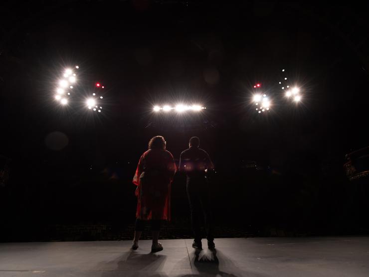 Two students standing on a dark stage beneath multiple spotlights