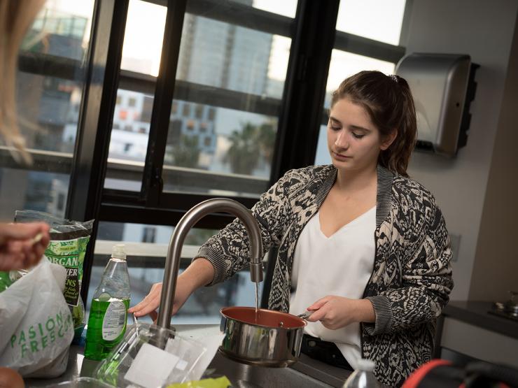 Student in the kitchen space rinsing out pot in the sink