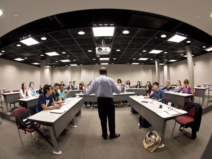 Fish-eye view from the front of a classroom, with a lecturer standing at the front of the class