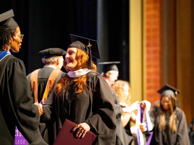 A graduate student receiving their degree at their hooding ceremony on stage, shaking the hand of a faculty member