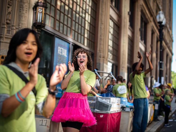 Students of diverse backgrounds in matching green shirts clap and celebrate on the sidewalk 