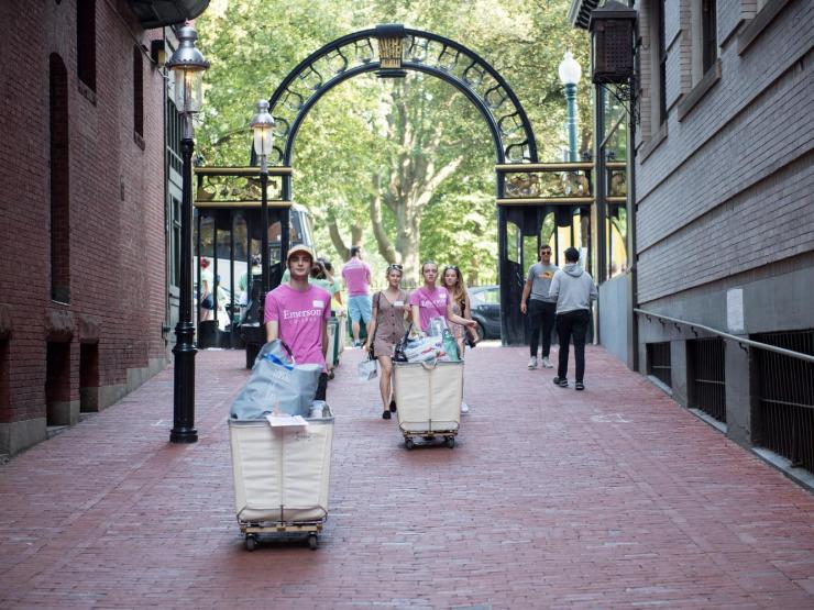 Students pushing carts on wheels down brick sidewalk.