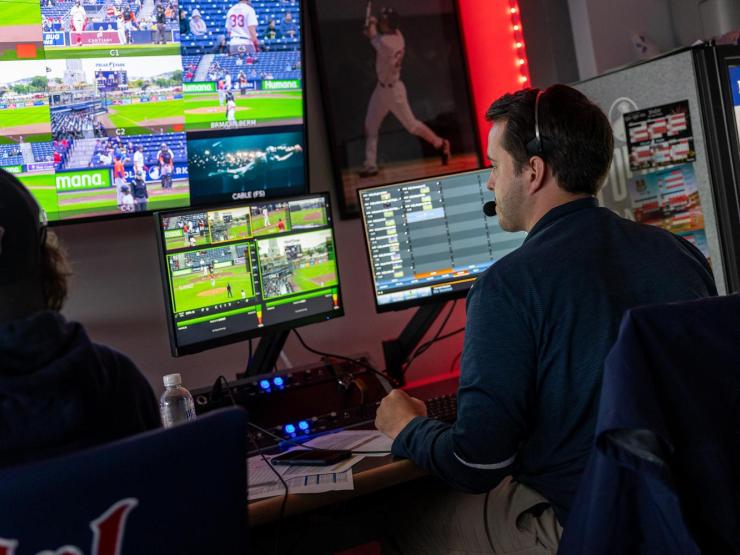People working at a broadcast desk, looking at monitors during a sports event