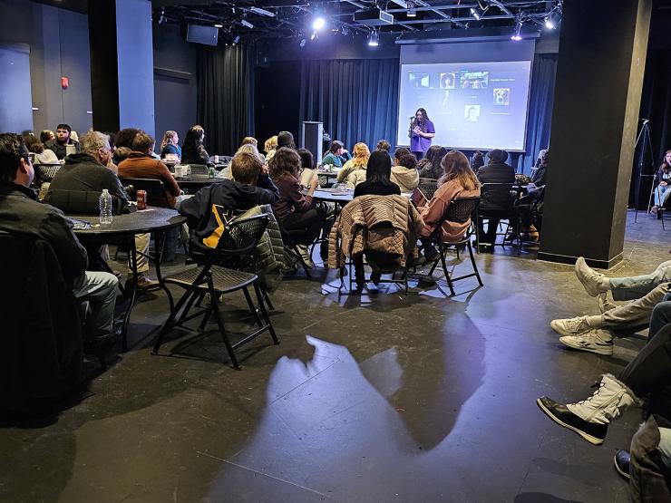 An audience in chairs, seated in front of a stage for a reading performance