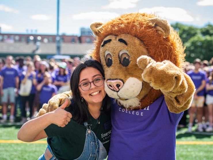 A student giving a thumbs up and smiling next to Griff, Emerson College's mascot, a big lion wearing a purple shirt