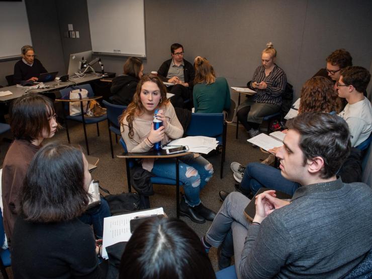 Students seated in groups within a classroom, having a discussion at their desks