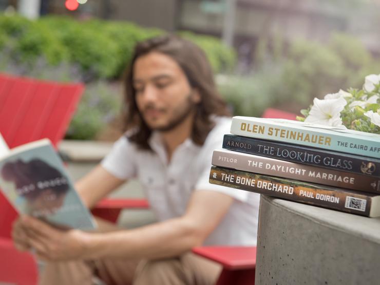 A student reading a book with a stack of books in the foreground