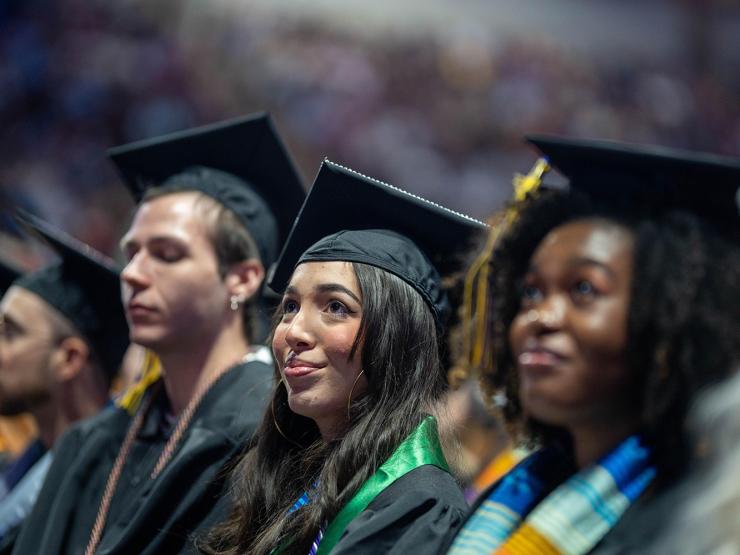A student wearing a cap and gown during their graduation ceremony, smiling