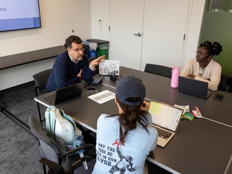 Three people engaged in a discussion around a conference table with laptops and notes.