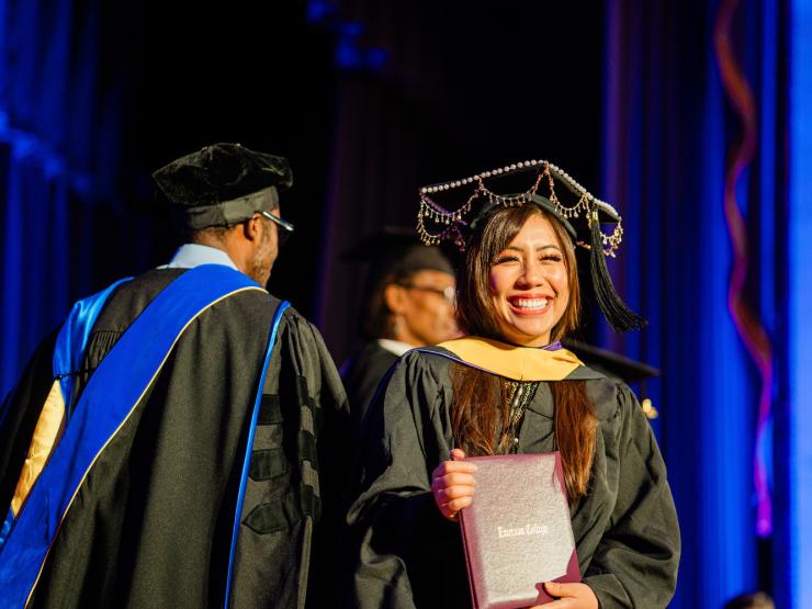 A student smiling widely while wearing regalia during their Graduate Hooding Ceremony