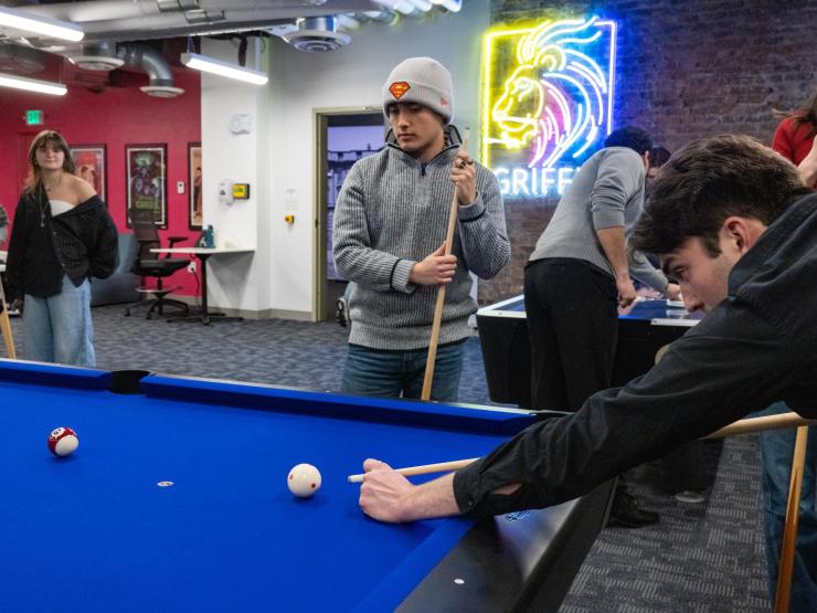 Students playing pool, one student takes their turn, the other waits with cue