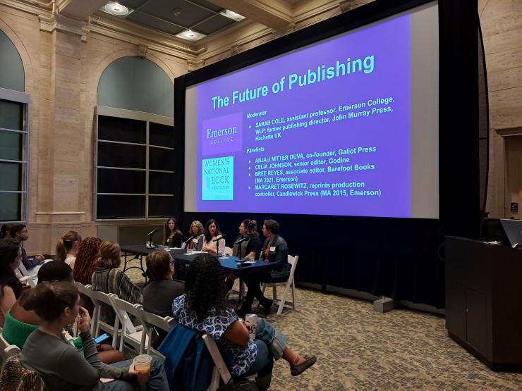 Panel discussion titled “The Future of Publishing” projected on a large screen at the front of a lecture hall. Four speakers sit at a table with microphones while an audience listens from white folding chairs. Logos for Emerson College and the Women’s National Book Association appear on the slide.