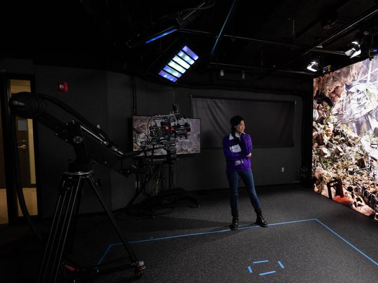 A student wearing an Emerson scarf while observing some footage in a production studio, standing in front of a large projector screen