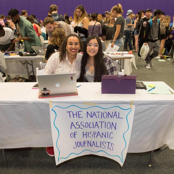 Two students sitting at a booth at the student org fair