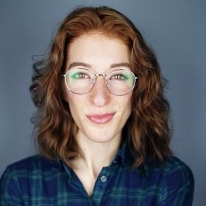 Photo of Joy facing the camera in a plaid shirt, wearing glasses