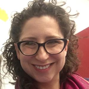 smiling face of a white woman with brown curly hair and glasses