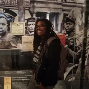 A photograph of Letta Neely in front of a Voices of Protest and Resistance display