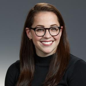 White woman with long, straight dark brown hair and glasses wearing a black turtleneck.