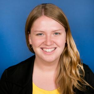 Danielle is smiling at the camera. She has blond hair, a yellow top, and a professional blazer.