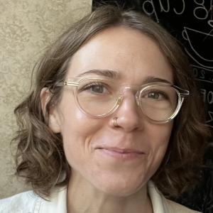 Photo of Channing - a young white woman with brown wavy hair and clear rimmed glasses