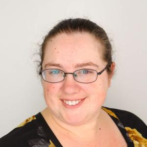 smiling white woman with glasses, dark hair, wearing a black shirt with large yellow flowers