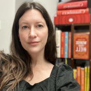 White woman with long, brown hair sitting in front of books