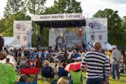 People sitting on lawn watching a concert on stage with banner that says "Boston Art & Music Soul"