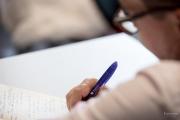Close-up of a person’s hand writing on paper with a purple Emerson pen