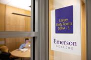 A photo of a sign labeling a study room in the Iwasaki Library. A student is inside the room on their laptop, out of focus.