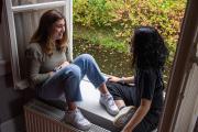 2 students sit on the window ledge talking