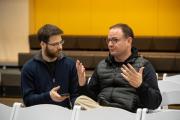 A news interview between two men, with one recording the other using a smartphone