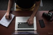 Close up of student's hands while simultaneously taking notes on paper and working at laptop