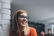 Woman smiling, wearing an orange shirt and glasses