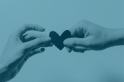 A photo of two hands holding a paper heart with a light blue overlay