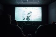 audience members look toward large movie screen in dark room