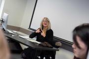 Teacher in glasses and ascot in front of a class signs in ASL